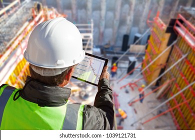 civil engineer or architect with hardhat on construction site checking schedule on tablet computer