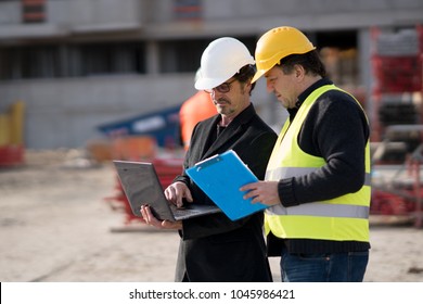 Civil Engineer Giving Instructions To A Construction Worker Using A Computer Laptop. Outdoors