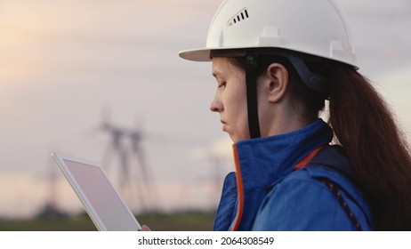 Civil Engineer, Power Engineer Woman In Protective Helmet, Building And Repairing Power Lines, Using A Computer Tablet. An Employee Of An Electric Utility Company Working Outdoors Serving Power Lines.