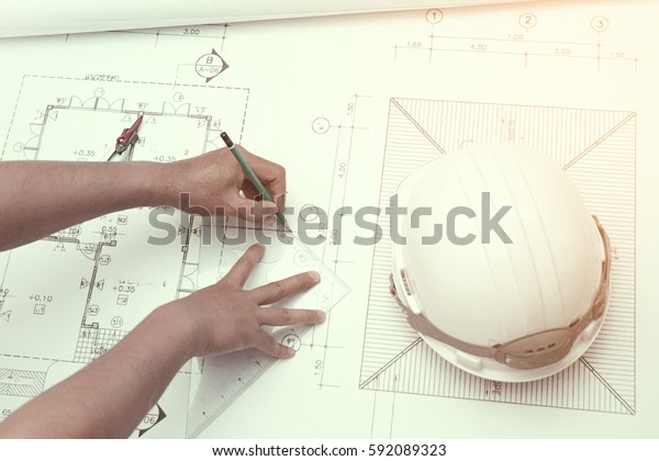 Civil engineer\
tools during worked at home office with white safety helmet\
,divider,ruler and blue\
print.\
