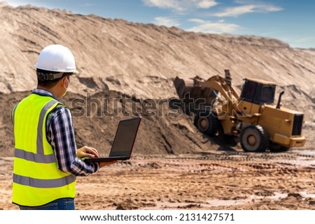 A Civil engineer using laptop to inspect work of Yellow Excavator working at sandpit. sand industry.