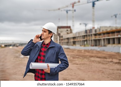 civil engineer in a white helmet with documents in his hands talking on the phone on the background of construction. natural light.