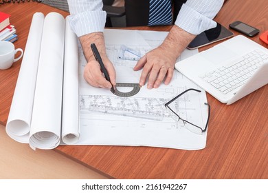 A Civil Engineer Is Working On An Industrial Building Construction Project. The Engineer Is Leaning Over The Table And Making Changes To The Drawings.