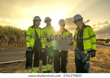Civil engineering contractors coordinating wind farm site operations during golden hour. Professional project management team reviewing blueprint logistics for utility infrastructure.