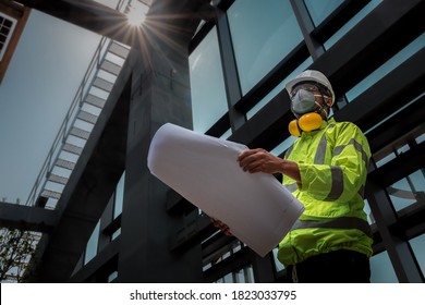 Civil Engineering People Wearing Face Mask And Safety Helmet On Construction Site Holding Blueprint In His Hand. Building Inspector. Construction Site Check Drawing And Business Workflow Of Building