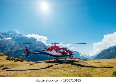 Civil helicopter landed in high altitude Himalayas mountains. Thamserku 6608m mountain on the background. Namche Bazaar, Nepal. Safety air transportation and travel insurance concept image.