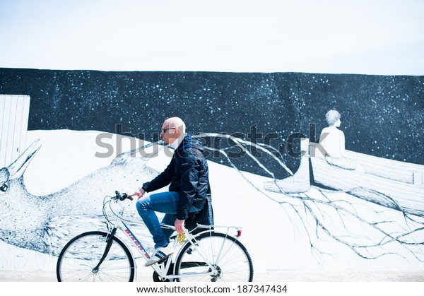 CIVITANOVA MARCHE, ITALY-APRIL 13, 2014:An
unidentified man on a bike in front of a graffiti of project 