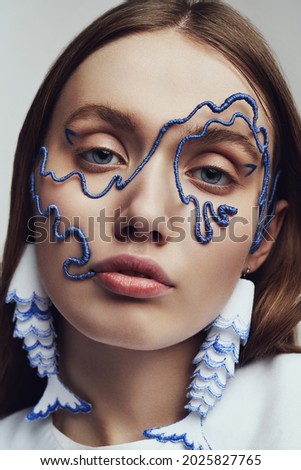 Ckose up portrait of woman in blue wire mask and with blue and white fish earrings. Creative accessories on marine theme                                                     
