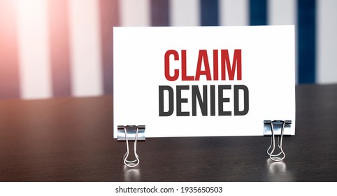 CLAIM DENIED sign on paper on dark desk in sunlight. Blue and white background - Shutterstock ID 1935650503