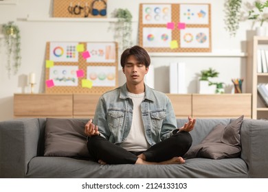 Clam Of Asian Young Man Doing Yoga Lotus Pose To Meditation And Relax On Couch During Work Online At Home.Happiness Male Break After Worked Close Him Eyes And Deep Breath With Yoga So Peaceful.