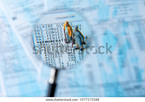 Clamart, France - April 25, 2021: French payroll seen in detail through a magnifying glass showing social security contributions for retirement and sickness, with small figurines of the elderly