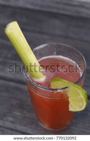 A Clamato drink with celery, salt and line in a pint glass sitting on an old wood deck.