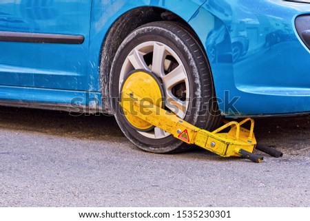 Clamped front wheel of illegally parked car, yellow clamp attached to wheel