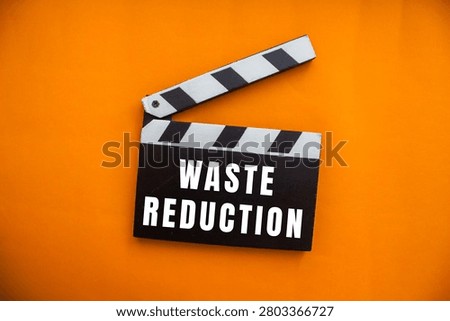 Clapperboard displaying waste reduction on an orange background, symbolizing environmental action and sustainability initiatives