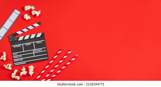 A clapperboard, film strip, popcorn and straws lie on the left against a red background with copy space on the right, top view - large shot. Cinema love and valentine's day concept.