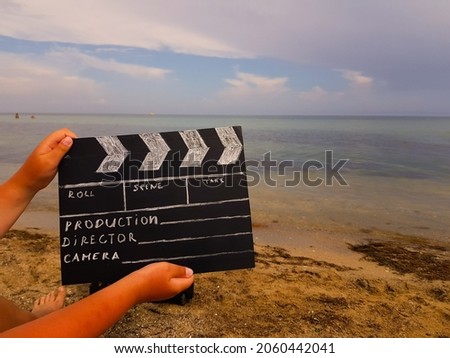 a clapperboard for filmer production in the hands of a man against the background of a sandy beach and the sea. summer