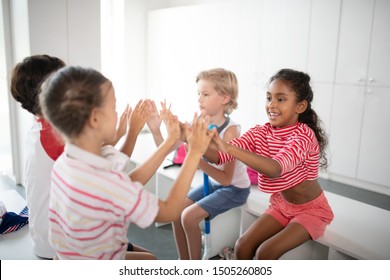 Clapping hands. Cute cheerful boys and girls clapping their hands while sitting in locker room - Powered by Shutterstock