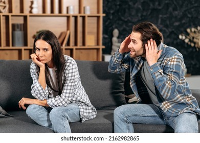 Clarification of relations between spouses. Caucasian couple sitting on sofa in living room, quarreling over disagreement, man yelling at woman, woman experiencing psychological abuse from her husband
