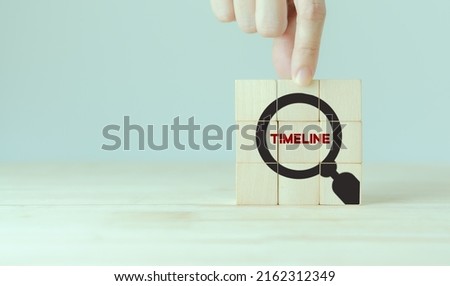 Clarifying project timeline concept. Project management, scheduling, milestones setting. Wooden cubes with magnifyier timeline text icon on grey background. Project planning presentation.