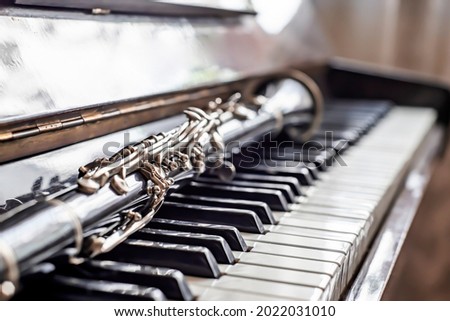 The clarinet lies on the piano keys by the window.