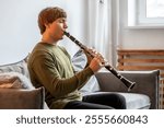 Clarinet player. Concentrated man clarinetist playing flute woodwind music instrument sitting on couch at home. Musical instruments. Focused guy plays the oboe in living room. Relaxed mental hobby.