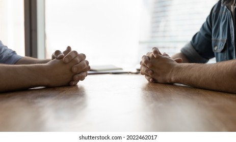 Clasped hands of two businessmen, business partners, competitors sitting opposite at office conference table. Professional leaders meeting for negotiation, conversation, dialogue, interview. Close up