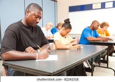 Class of adult college students taking a test.  Focus on guy in front left.