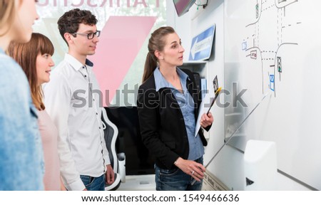 Class in driving school analyzing complex traffic situation on white board, the group standing around the teacher