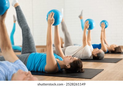 Class of male and women of different ages in active wear pressing balls in hands exercise during Pilates training together in gym - Powered by Shutterstock