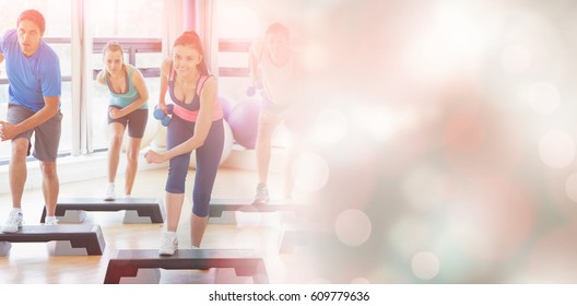 Class performing step aerobics exercise with dumbbells at gym