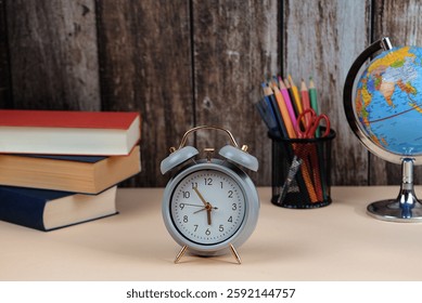 A classic alarm clock is sitting prominently on a wooden desk next to a few books and a detailed globe showcasing various countries