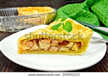 Classic American apple pie with mint leaves in a plate, a napkin, a glass form on a wooden boards background