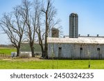 Classic Amish farmstead with a large barn and silo standing on a sprouting spring field under a clear blue sky in Lancaster, Pennsylvania. High quality photo. PA US North America