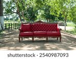 A classic antique red leather sofa on a dirt road with wooden railings at the entrance to a farmhouse