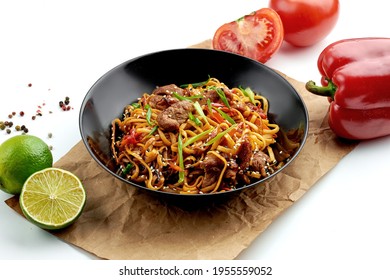 Classic Asian street food - udon wok noodles with pork, vegetables in sweet and sour sauce, served in a black plate. white background