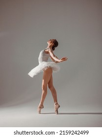 classic ballet posing. young slim dancer, fit girl ballerina stands in white ballet tutu like white swan in profile in pointe shoes on white wall background in studio light. ballet concept, free space - Shutterstock ID 2159242499