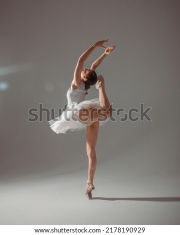 classic ballet posing. young slim dancer, fit girl ballerina is making trick in white ballet tutu like swan in white pointe shoes on white wall background in studio light. ballet concept, free space