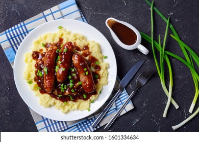 classic Bangers and Mash with Onion Gravy sprinkled with spring onion on a plate on a concrete table, english cuisine, flat lay