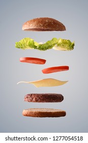 Classic beef burger floating with ingredients broken down in parts on gray gradient isolated background. Front view. Vertical composition.