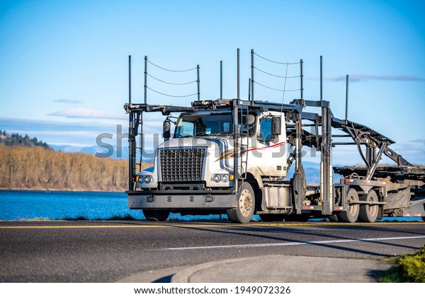 Classic\
Big rig industrial car hauler semi truck with empty double deck\
hydraulic modular semi trailers running on the narrow road along\
the river to warehouse for pick up next cars\
load
