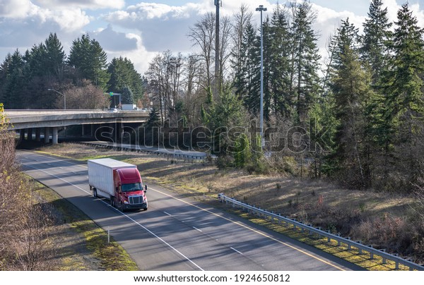 Classic big rig red semi truck tractor with\
sleeping compartment transporting commercial  cargo in dry van semi\
trailer moving on the highway road intersection with one way\
traffic direction