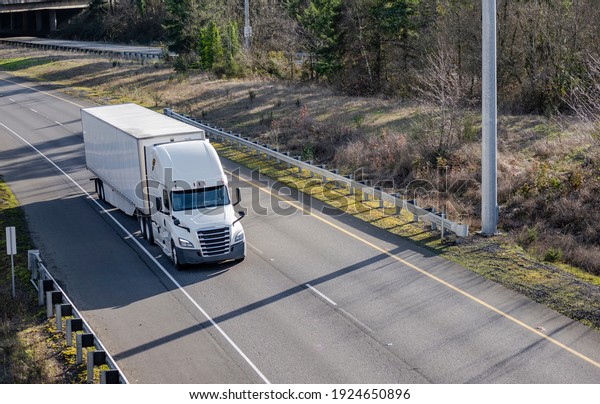 Classic big rig white semi truck tractor with\
sleeping compartment transporting commercial  cargo in dry van semi\
trailer moving on the highway road intersection with one way\
traffic direction\
