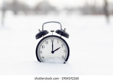 A Classic Black Alarm Clock In The Snow. Time Is 2 Hours On The Clock.