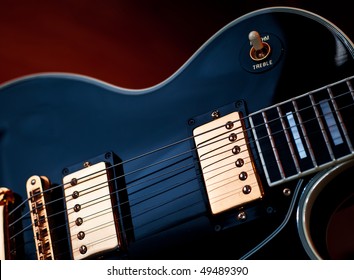 Classic black Les Paul rock and roll or jazz style guitar. Soft blue lighting on guitar and warm background light creates stage or studio performance atmosphere.