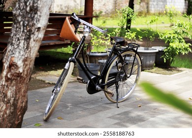 A classic black vintage bicycle with leather saddle and unique front design, parked on a paved area in a lush garden. The serene setting includes potted plants, a wooden bench, and natural greenery - Powered by Shutterstock