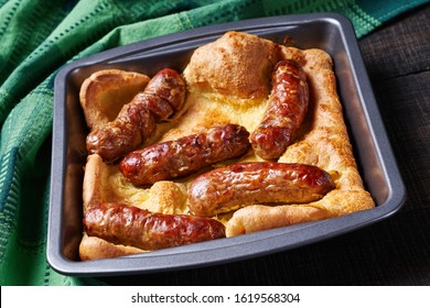 Classic British Dish Toad In The Hole Of Yorkshire Pudding With Roasted Sausages Served On A Square Cake Pan On A Dark Rustic Wooden Background, Horizontal View, Close-up