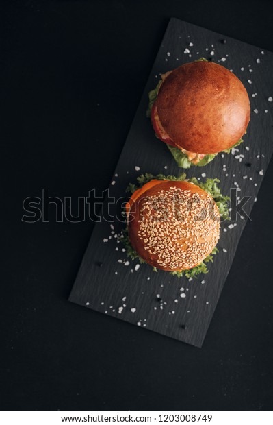 Classic\
burgers with becon, meat, cheese, onion, tomato and cheese and\
integral bun. On textured black board. Flat\
lay.