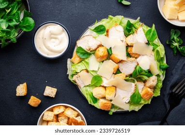 Classic Caesar salad with chicken, iceberg salad, croutons, parmesan cheese and caesar dressing. Black table background, top view