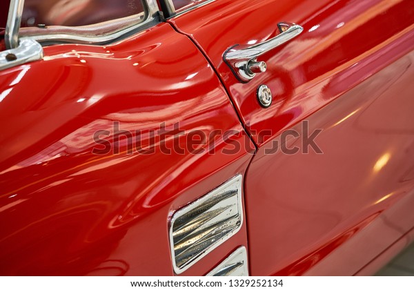 Classic car background. Close up of shiny\
red paint chrome door handle & side grill. Vintage car\
wallpaper. Reflection on bonnet & chrome of retro vehicle. Old\
automotive restoration & auto\
detailing.