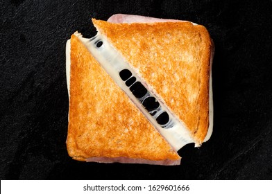 Classic cheese and ham toasted sandwich cut in half isolated on black cast iron griddle. Top view.